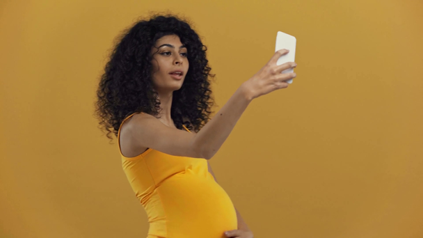 mujer embarazada bi-racial sonriente tomando selfie aislado en amarillo oscuro
 - Metraje, vídeo