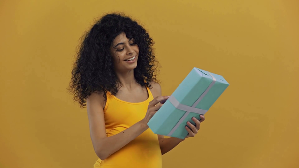 happy bi-racial pregnant woman showing gift box isolated on dark yellow - Metraje, vídeo