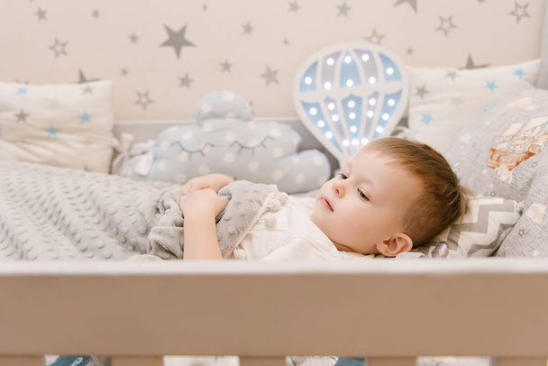 Little cute baby boy lies in the children room in a wooden bed h - 写真・画像