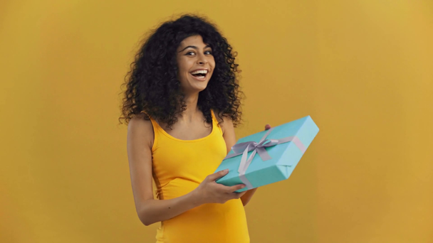 happy bi-racial pregnant woman taking gift box isolated on dark yellow - Felvétel, videó