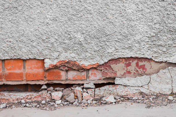 The foundation of a residential building is gradually collapsing. Cracks in the foundation. Plaster falling off of a brick wall due to the impact of weather factors. - 写真・画像