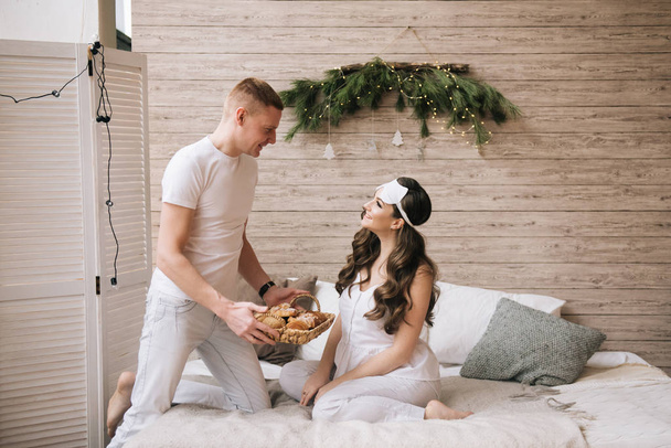 Beautiful young, stylish pregnant girl with husband having Breakfast croissants in bed - Foto, Imagem