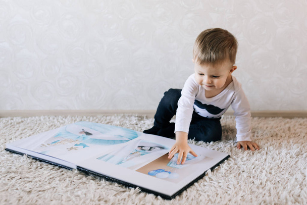 Cute baby sitting and looking at a large stylish photo book with their photos. Children's photo album - Fotografie, Obrázek