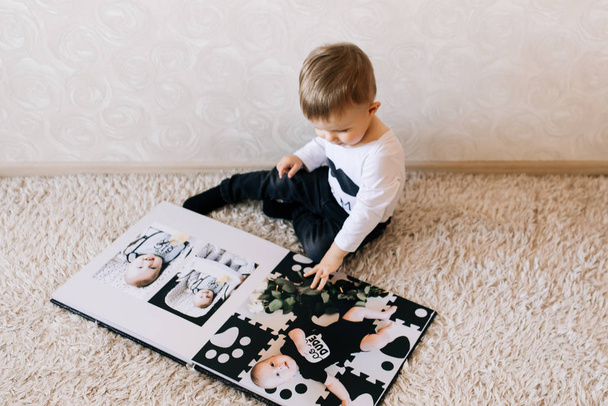 Cute baby sitting and looking at a large stylish photo book with their photos. Children's photo album - 写真・画像