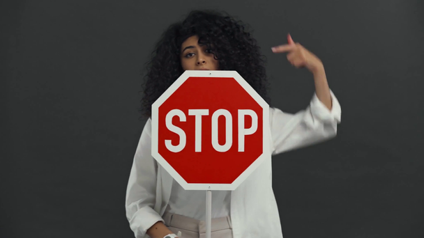 mujer bi-racial escéptica sosteniendo cartel de stop aislado en negro
 - Imágenes, Vídeo