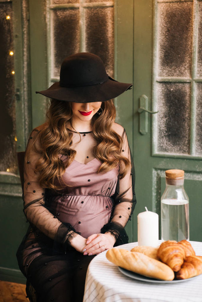 Красива молода, стильна вагітна дівчина в чорній сукні, в інтер'єрі французької пекарні. - Фото, зображення