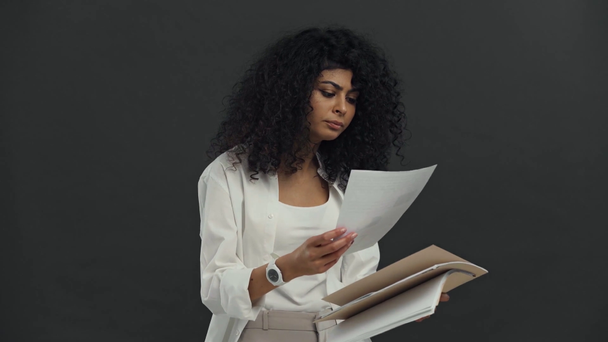 серьезная двурасовая деловая женщина читает документы изолированные на черном
 - Кадры, видео