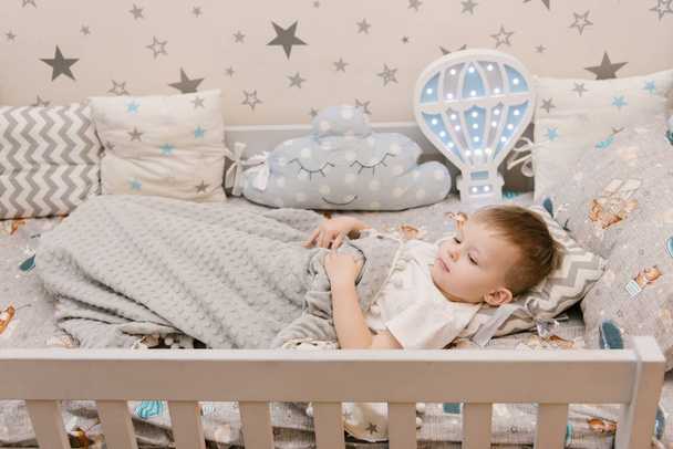 Little cute baby boy lies in the children room in a wooden bed h - Фото, зображення