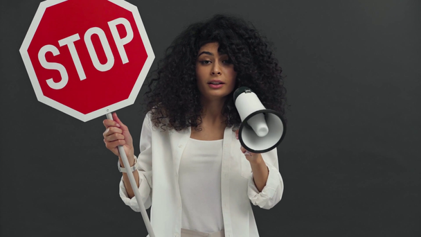 με αυτοπεποίθηση δικοφυλετική γυναίκα με stop placard μιλώντας σε μεγάφωνο απομονωμένο σε μαύρο - Πλάνα, βίντεο