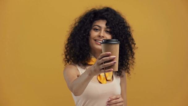 wesoły bi-rasowy kobieta pokazując kawa iść odizolowany na ciemny żółty - Materiał filmowy, wideo