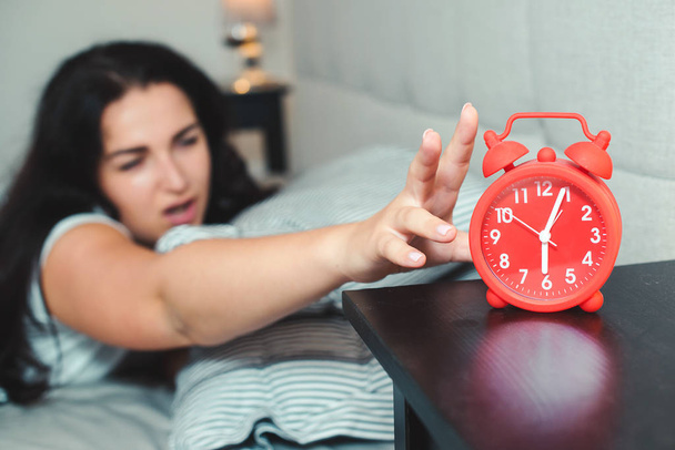 Sleepy woman reaching to the alarm clock in the morning with late wake up. Asleep girl stopping alarm clock - Fotoğraf, Görsel
