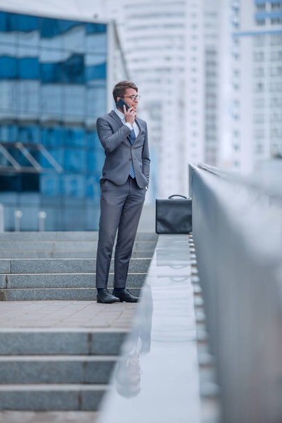 businessman talking on smartphone while standing on steps outdoors - Valokuva, kuva