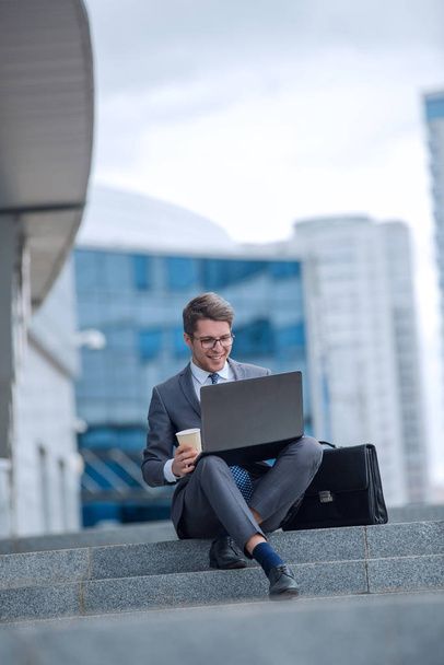 business man using his laptop sitting on the steps on a city street - Fotó, kép