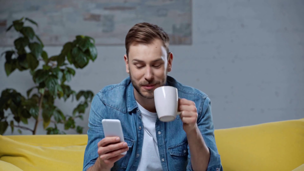 smiling man drinking coffee and making online bets - Video, Çekim