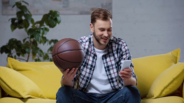 smiling sports fan holding basketball and making online bets - Footage, Video