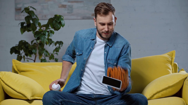 veselý muž v baseballové rukavici hrát s chytrým telefonem - Záběry, video