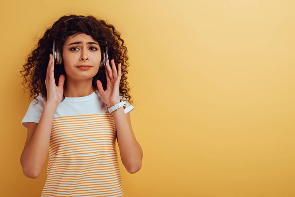 upset bi-racial girl listening music in headphones on yellow background - Foto, immagini