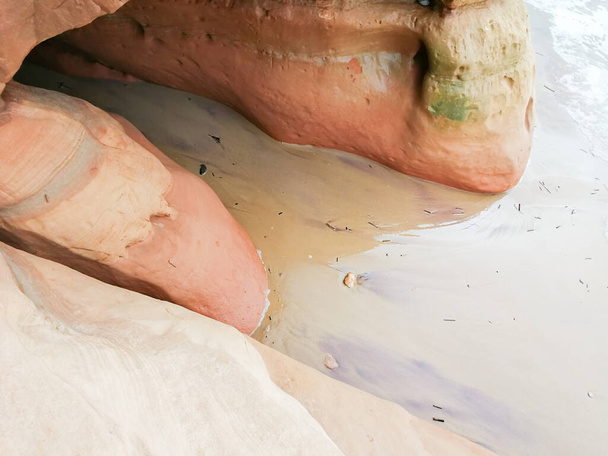 バルト海沿岸のオレンジ砂岩の崖。12月の石灰岩のビーチや洞窟を洗う海の波。ラトビアの海岸線にある砂岩の崖や洞窟.  - 写真・画像