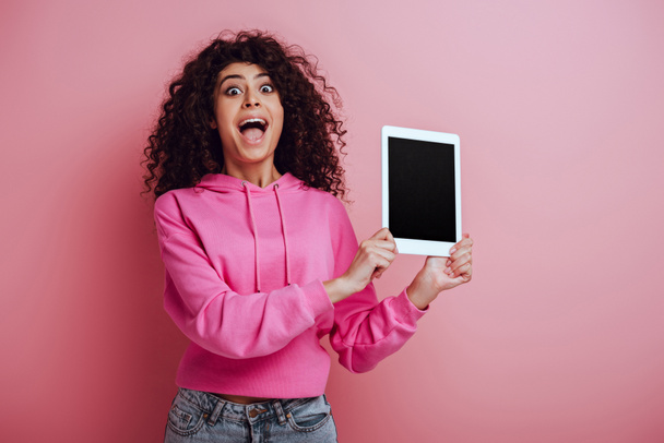 šokované bi-rasové dívka ukazuje digitální tablet s prázdnou obrazovkou na růžovém pozadí - Fotografie, Obrázek