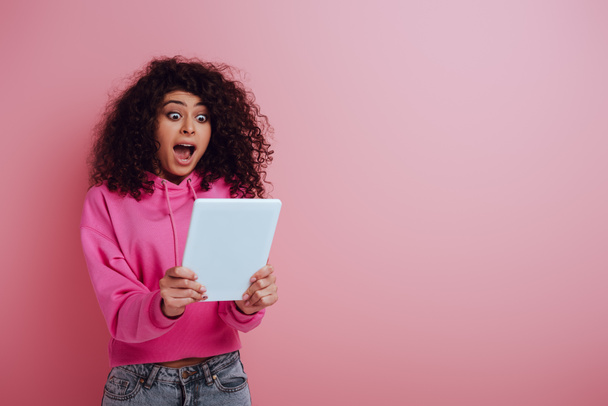 conmocionada chica bi-racial mirando tableta digital sobre fondo rosa
 - Foto, imagen