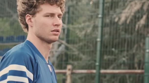 Side view of Cool curly handsome basketball player looking away and talking something while walking on basketball court outdoors - Imágenes, Vídeo