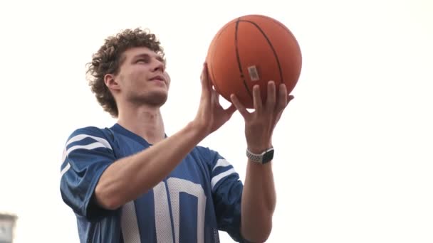 View from below of Smiling curly handsome man playing basketball on basketball court outdoors - Video, Çekim