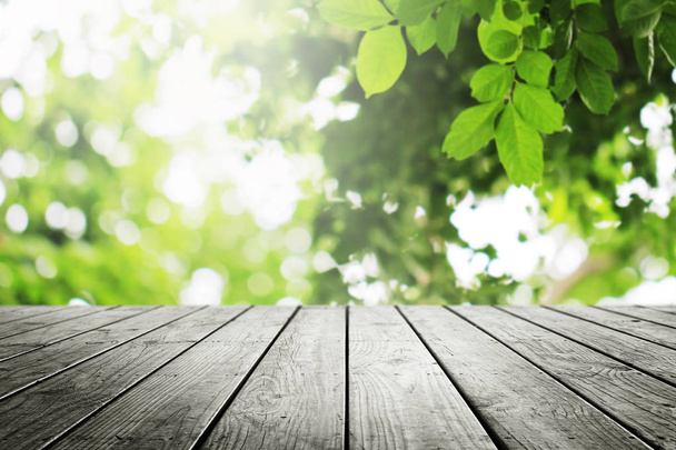 Holztisch mit schönem Sonnenlicht und unscharfen grünen Blättern Natur im Garten Bokeh Hintergrund. - Foto, Bild