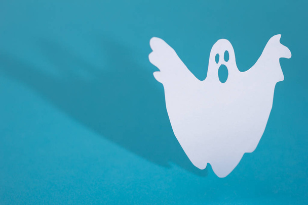 Halloween háttér dekoráció ünnep koncepció. Vicces szellem csinál boo gesztus és grafikus árnyalat mögött kék asztal. - Fotó, kép