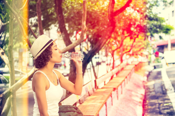 Warme zomerdag, vrouw die water drinkt op de bank. Beboste oppervlakte beschermd door schaduw. - Foto, afbeelding