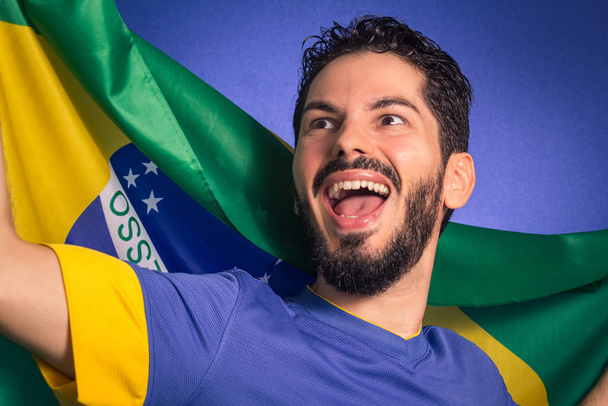 Brazilian soccer football team player. One supporter and fan holding Brazil flag. Wearing blue uniform on blue backdrop. - Photo, Image