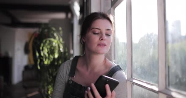 Young adult female checking smartphone in morning sunshine - Filmmaterial, Video