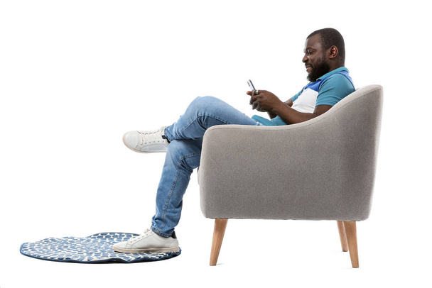 Афроамериканец с мобильным телефоном сидит в кресле на белом фоне
 - Фото, изображение