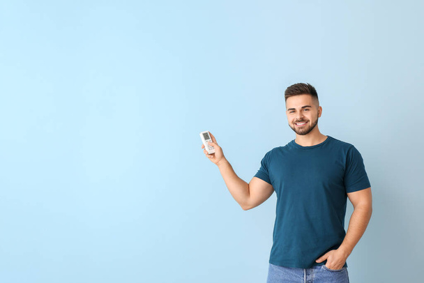 junger Mann mit Klimaanlage-Fernbedienung auf farbigem Hintergrund - Foto, Bild