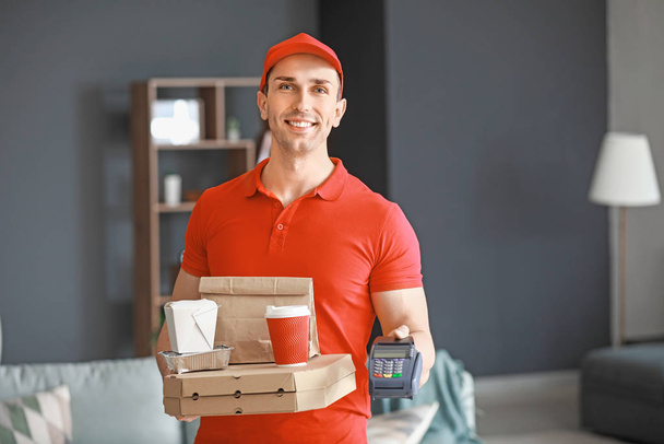 Handsome worker of food delivery service with payment terminal indoors - Photo, Image
