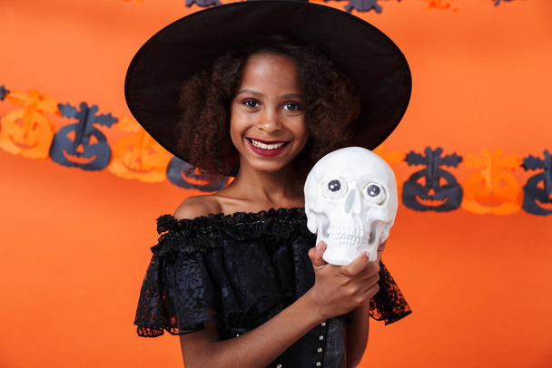 Image of joyful african american girl holding toy skull and smiling - Фото, изображение