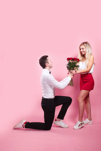 Guapo elegante chico está proponiendo a su hermosa novia, dándole rosas y sonriendo
 - Foto, imagen