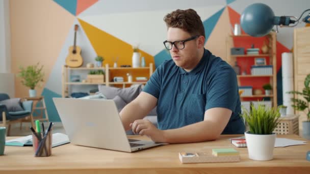 Slow motion of serious young man working at home using laptop concentrated on work - Materiał filmowy, wideo