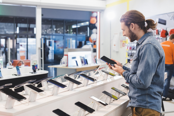 side view of smiling man holding smartphone in home appliance store  - 写真・画像