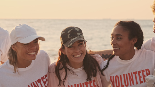 Pozytywnie uśmiechnięci młodzi wolontariusze zostają razem podczas robienia zdjęć nad morzem wczesnym rankiem - Materiał filmowy, wideo