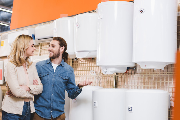 sorrindo namorado e namorada falando perto de caldeiras na loja de eletrodomésticos
  - Foto, Imagem