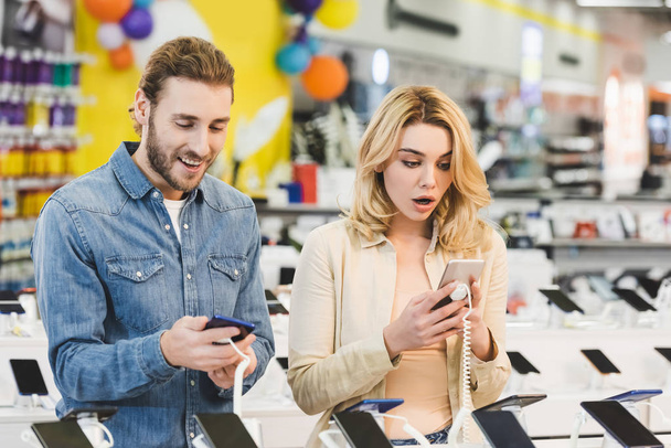 sorprendido novio y novia mirando nuevos teléfonos inteligentes en la tienda de electrodomésticos
  - Foto, imagen