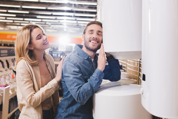 novio sonriente tocando caldera y novia mirándolo en la tienda de electrodomésticos
  - Foto, imagen