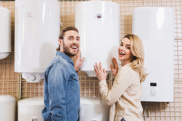 smiling boyfriend and girlfriend touching boiler in home appliance store  - Zdjęcie, obraz