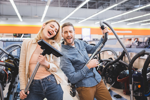 boyfriend playing with vacuum cleaner and girlfriend singing in home appliance store  - Fotografie, Obrázek