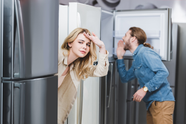 foco seletivo de namorada curiosa e namorado olhando para geladeira em segundo plano na loja de eletrodomésticos
  - Foto, Imagem
