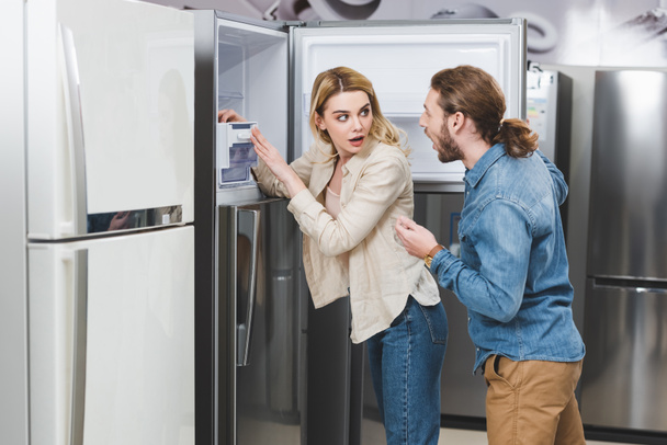 Ev aletleri dükkanında buzdolabının yanında duran şok olmuş sevgili ve sevgili.  - Fotoğraf, Görsel