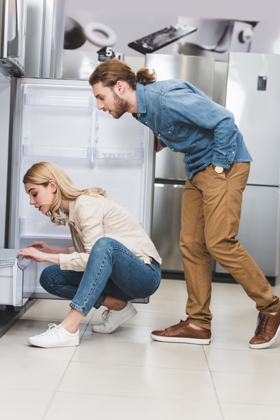side view of boyfriend and girlfriend looking at fridge in home appliance store  - Foto, Bild
