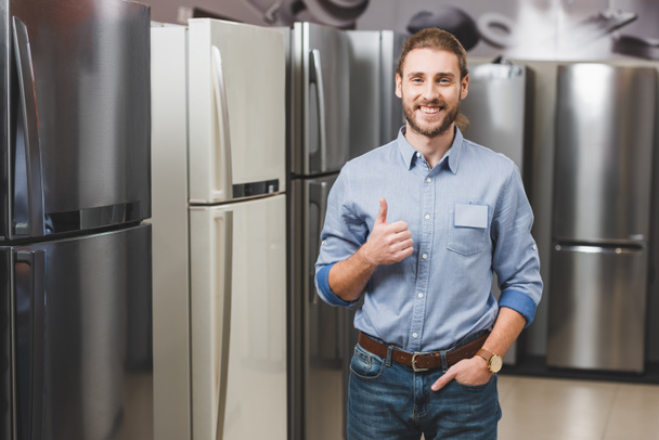Lächelnder Berater wie in der Nähe von Kühlschränken im Haushaltsgerätehaus  - Foto, Bild