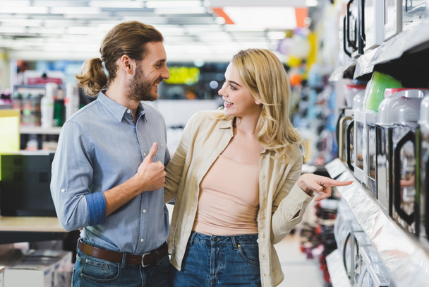 consultor sonriente mostrando como y mujer señalando con el dedo en el microondas en la tienda de electrodomésticos
  - Foto, imagen