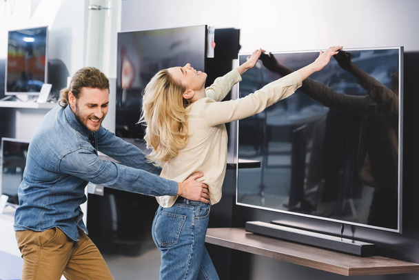 сердитий хлопець тягне дівчину з телевізором в магазині побутової техніки
  - Фото, зображення